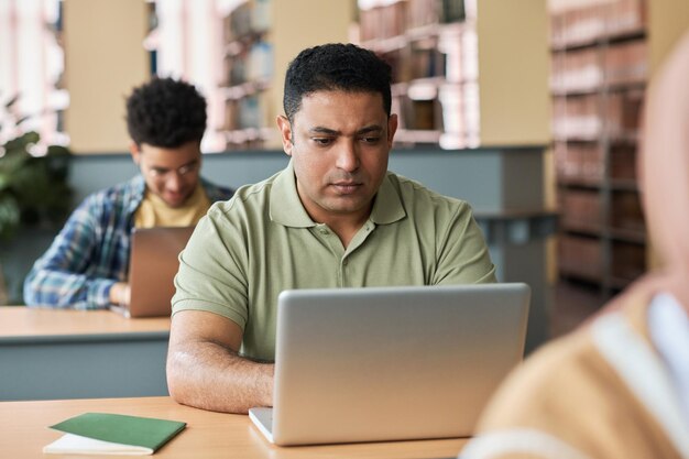 Estudiante adulto sentado en el escritorio y usando una computadora portátil en la lección con otros estudiantes en clase