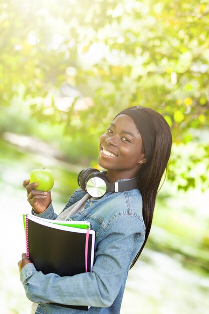 Estudiante africano sonriente que sostiene una manzana.