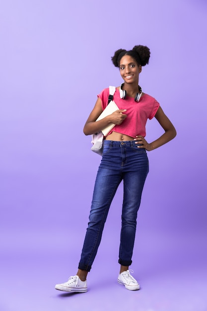 Estudiante afroamericana de longitud completa con mochila sosteniendo libro de ejercicios, aislado