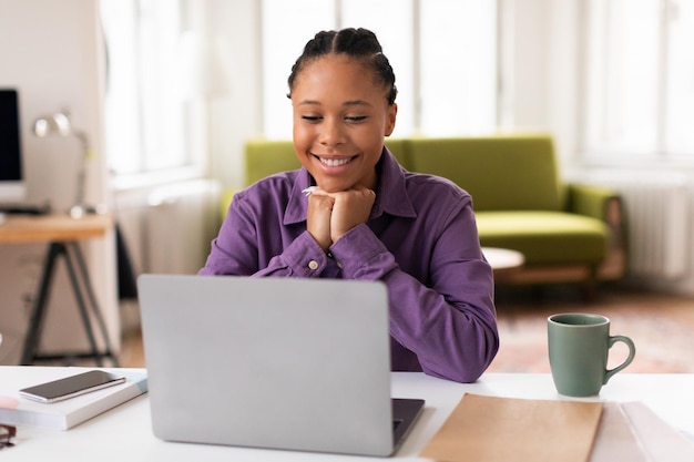 Una estudiante afroamericana sonriente con una computadora portátil disfrutando del aprendizaje en línea