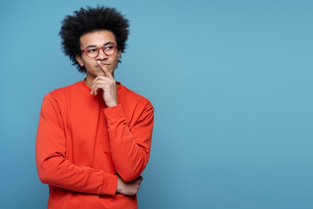 Estudiante afroamericano con anteojos sosteniendo el dedo cerca de la cara, buscando una solución creativa