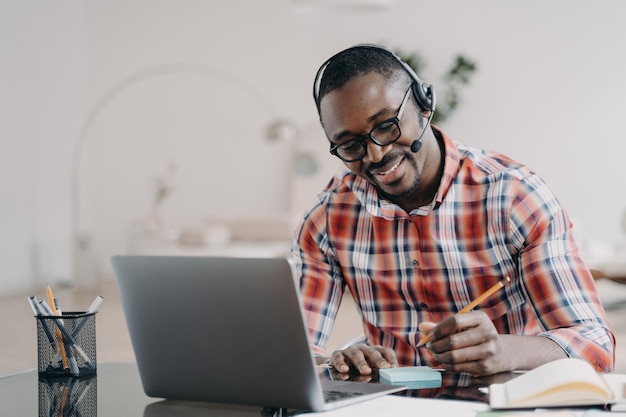Estudiante afroamericano en auriculares aprendiendo en una computadora portátil en línea toma notas Educación a distancia