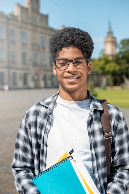 Estudiante afroamericano sonriente en vidrios con los libros.