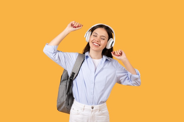 Estudiante alegre bailando con auriculares en un fondo amarillo
