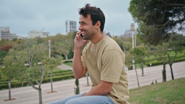 Estudiante alegre disfruta de la llamada riendo en el parque de la ciudad de cerca hombre hablando teléfono inteligente