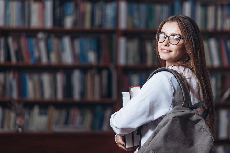 Estudiante alegre de pie en la biblioteca universitaria con libros
