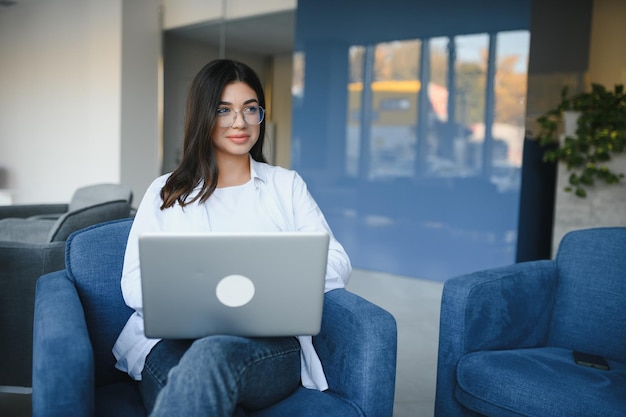 Una estudiante alegre que estudia en línea en un café usando una computadora portátil y auriculares en un espacio vacío