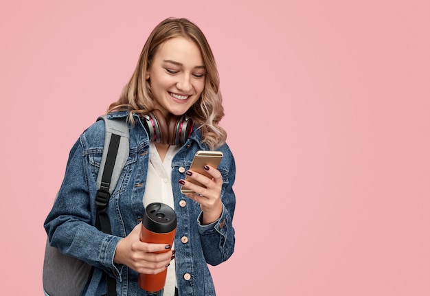 Estudiante alegre con termo con smartphone