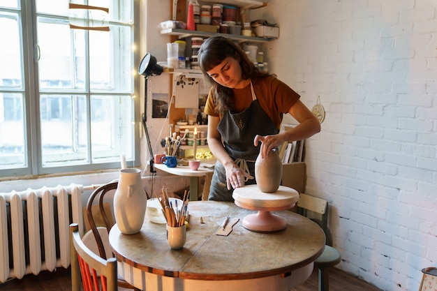 Estudiante de arte chica creativa o propietario del taller creando jarrón de alfarero en estudio trabajo femenino con arcilla