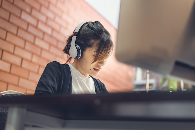 Estudiante asiática adolescente usa estudio de auriculares inalámbricos en línea. El estudiante mira el aprendizaje en línea de la computadora.