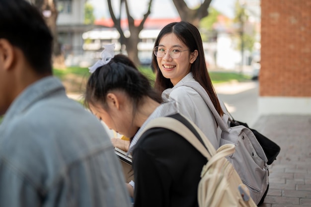 Una estudiante asiática positiva está sonriendo a la cámara sentada en una acera con sus amigas