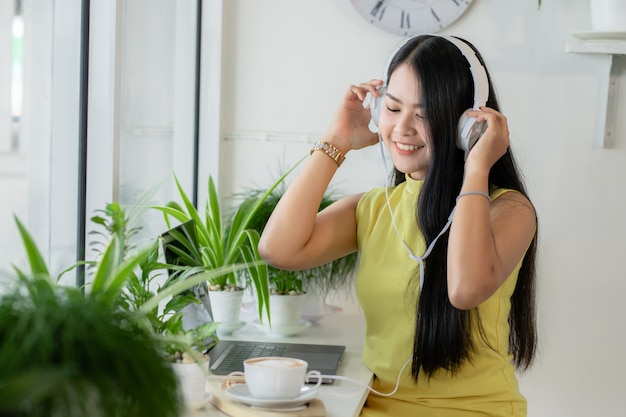 Una estudiante asiática sonriente usa auriculares inalámbricos para estudiar en línea con un maestro de Skype en una cafetería,