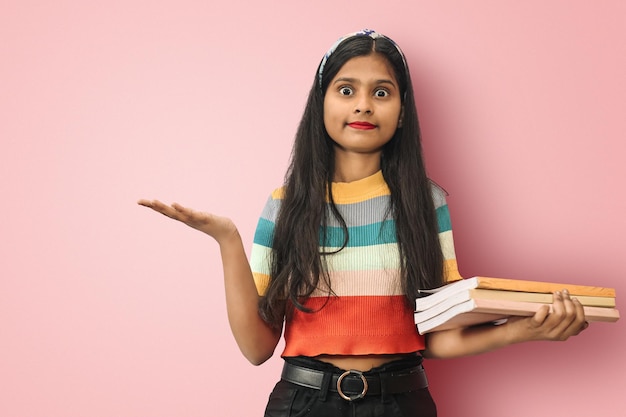 Estudiante asiática sorprendida sosteniendo libros y señalando con la otra mano con ojos grandes