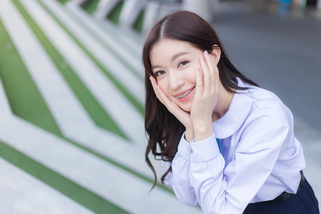 Una estudiante asiática con uniforme escolar se pone de pie y sonríe alegremente con aparatos ortopédicos en los dientes