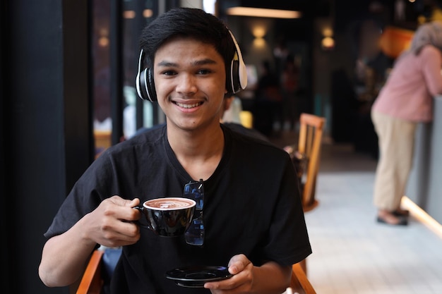Estudiante asiático beber una taza de café en la cafetería y sonriendo a la cámara