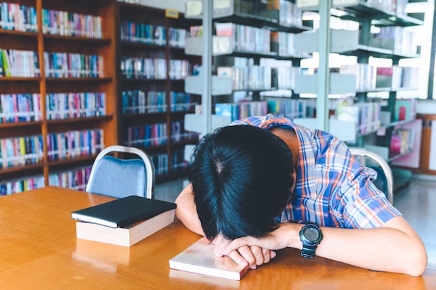 Estudiante asiático cansado durmiendo en el escritorio en una biblioteca