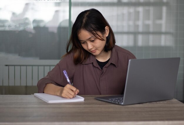 Estudiante asiático escribiendo material de punto de vista en Laptop