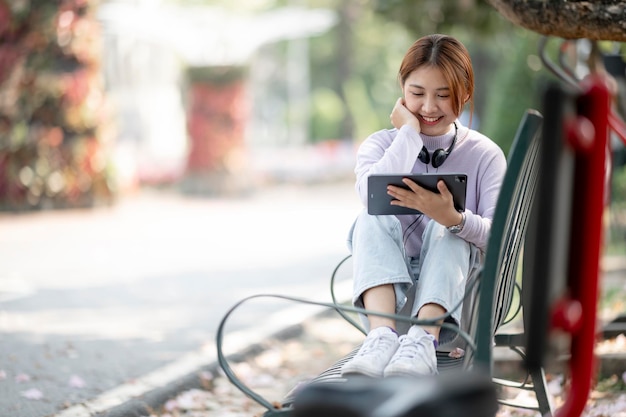 Estudiante asiático hermoso joven que usa la tableta digital al aire libre