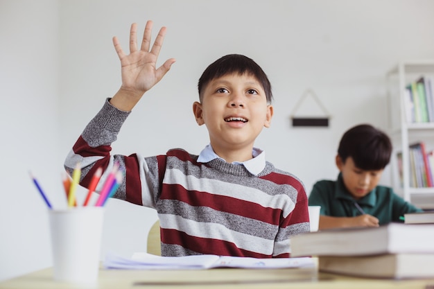 Estudiante asiático inteligente y activo levantando la mano durante la lección de clase para responder a la pregunta