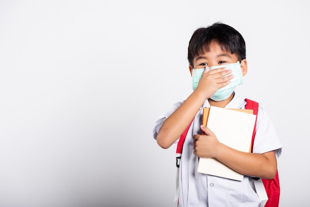 Estudiante asiático niño niño usa uniforme tailandés de estudiante y protección médica mascarilla y tapa de mano boca