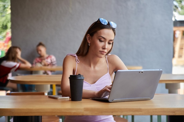 Estudiante asiático sentado en la mesa del café estudiando con un portátil haciendo los deberes