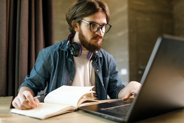 Estudiante barbudo con gafas estudiando con una laptop por la noche en el piso