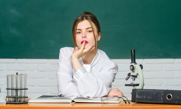 Estudiante de biología sentado en el fondo de la pizarra en el aula Mujer bastante adorable maestra o estudiante Químico biólogo con microscopio Estudiante inteligente Estudiar mucho Investigación científica Concepto de educación