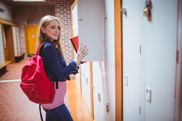 Estudiante bonita con la mochila que pone el cuaderno en el armario