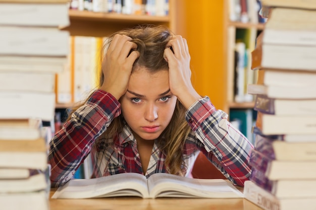 Foto estudiante bonita molesto estudiando entre pilas de libros