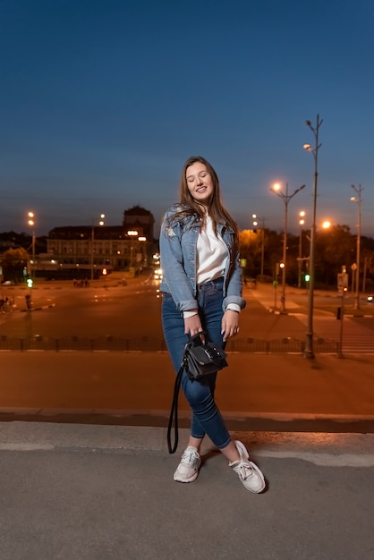 El estudiante camina por la ciudad al atardecer. Hermosa chica posando en la calle. Ropa juvenil. Marco vertical.