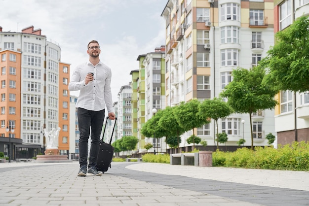 Estudiante caminando por la calle con taza de café y maleta