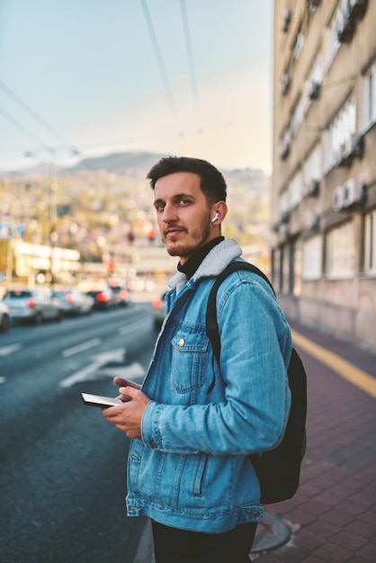 Un estudiante caminando por la ciudad llevando una mochila y usando gafas de sol mientras usa un