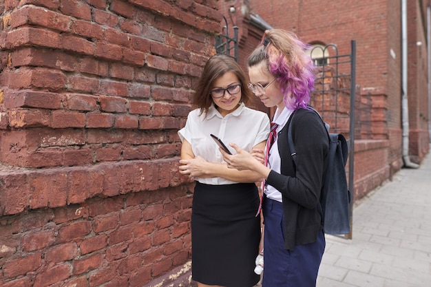 Foto estudiante caminando y hablando con maestra, niña mostrando en la pantalla del teléfono inteligente