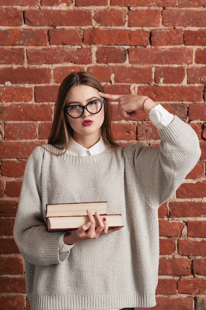 Estudiante cansado con libros muestra gesto de disparo