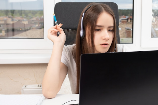 Foto un estudiante en casa se dedica a la capacitación, escucha atentamente y ve una conferencia en una computadora portátil con un micrófono en los auriculares