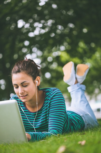 Foto estudiante casual contenido tirado en la hierba usando la computadora portátil