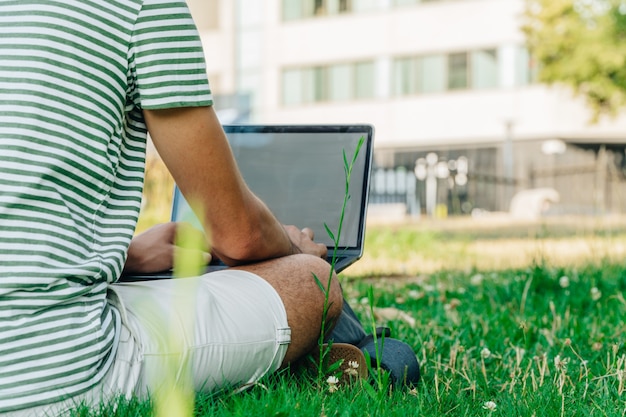 Estudiante caucásico irreconocible usando una computadora portátil en un parque