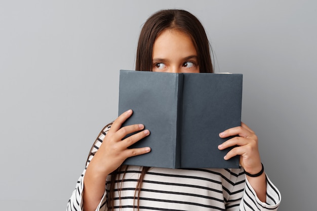 Estudiante chica adolescente sosteniendo un libro en sus manos sobre un fondo gris