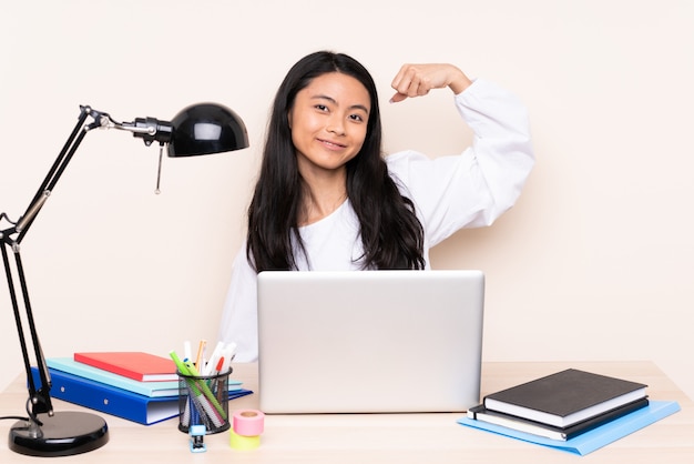 Estudiante chica asiática en un lugar de trabajo con una computadora portátil aislada en la pared de color beige haciendo un gesto fuerte