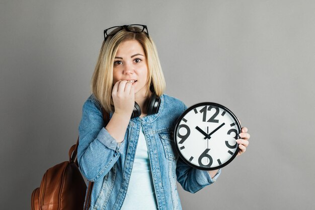 Estudiante chica con un gran reloj en las manos sobre un fondo gris