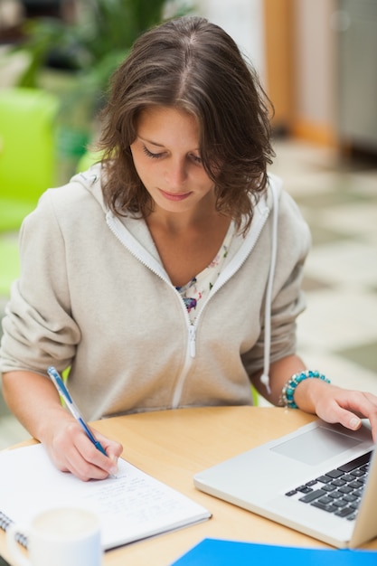 Estudiante concentrada haciendo la tarea por computadora portátil