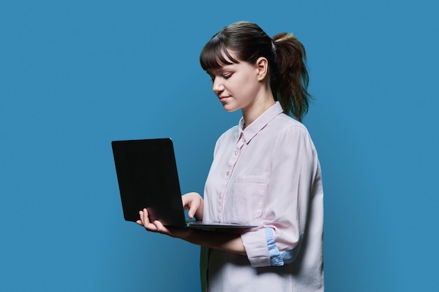 Estudiante concentrada y seria que mira la pantalla de su portátil en el fondo azul de un estudio chica inteligente inteligente que usa Internet para estudiar e-learning lecciones en línea cursos universitarios universitarios