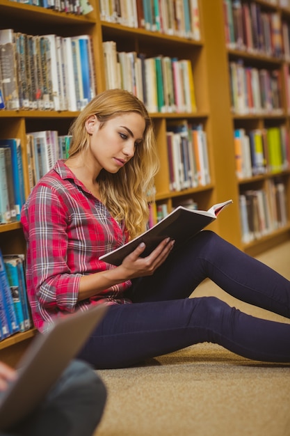 Estudiante concentrado que trabaja en piso en biblioteca