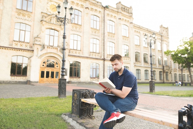 Estudiante concentrado sentado en el fondo de la universidad y leyendo un libro.