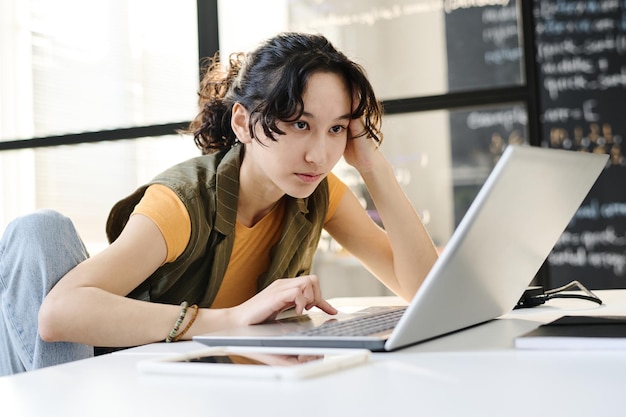 Estudiante concentrándose en su trabajo en línea en la computadora portátil ella sentada en el escritorio en el aula