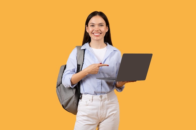 Estudiante confiada sosteniendo una computadora portátil y apuntando a la pantalla