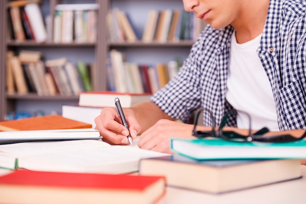 Estudiante confiado que estudia. Vista lateral del joven confiado haciendo investigación mientras está sentado en el escritorio en la biblioteca