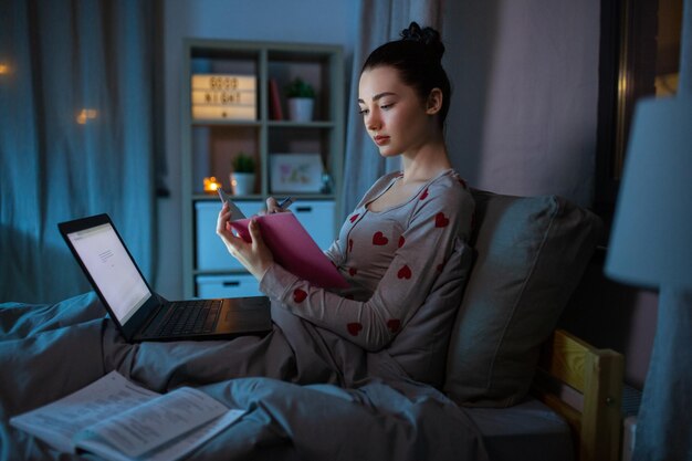 estudiante con cuaderno y portátil por la noche