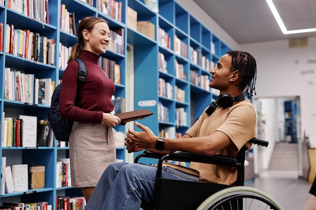 Estudiante con discapacidad hablando con un amigo en la biblioteca universitaria y sonriendo