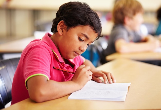 Estudiante de educación y niño en un aula escribiendo y estudiando para un examen de prueba y un cuaderno Escuela infantil masculina y niño con un lápiz de libro y creativo con desarrollo, crecimiento y aprendizaje